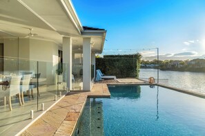 A modern outdoor pool area with clear water, a glass balustrade, and a view of a river. - Waters Edge Twin Waters - Pool, Deck & Kayaks (Coolum Region)
