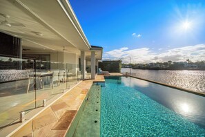 Een modern zwembadgedeelte met vrij uitzicht op een waterpartij, een glazen balustrade en een terras met tuinmeubilair.