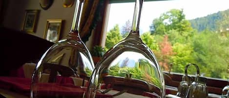 Two wine glasses on a table with a view of greenery outside.
