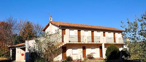 A two-story building with a tiled roof, a balcony on the upper floor, and a small attached structure to the left.