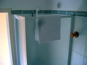 Un baño con una toalla blanca colgada en un perchero, una puerta de ducha y un muro de azulejos con un borde decorativo.