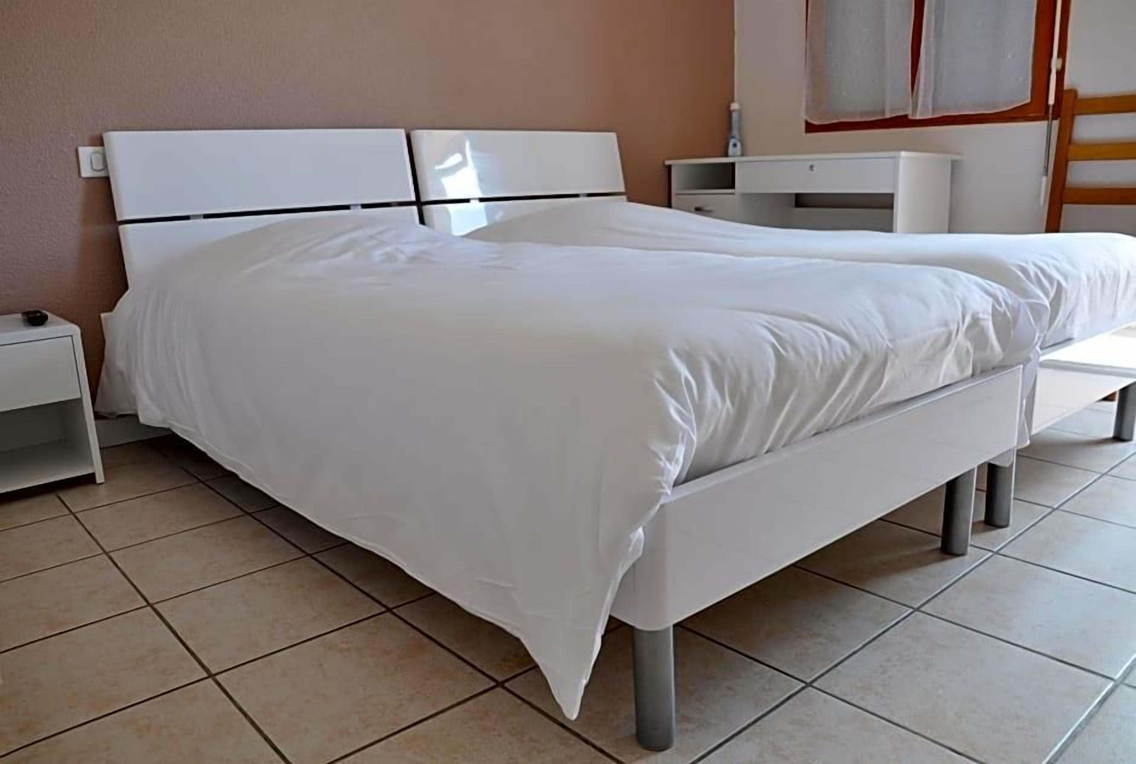 A single-bed room with a white headboard, a bedside table, and a nightstand.