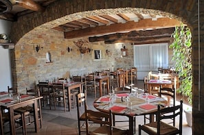 Un comedor rústico con paredes de piedra, vigas de madera y varias mesas dispuestas para comer.