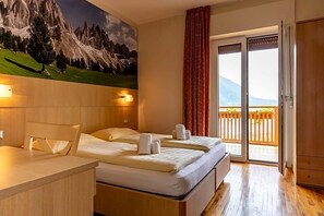 Quarto de hotel com cama, escrivaninha e vista para uma varanda com grade de madeira.
