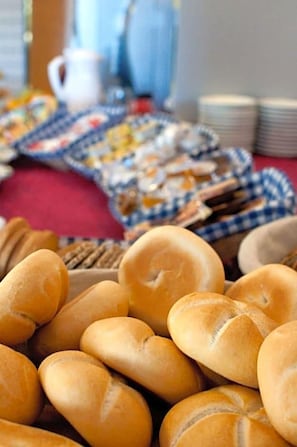 Una mesa con diversas opciones de panadería, incluyendo panes y pasteles, cubierta con un mantel azul y blanco a cuadros.