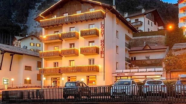 Un hotel con varios balcones, un cartel que indica que es el Hotel Lory y automóviles estacionados frente a él.