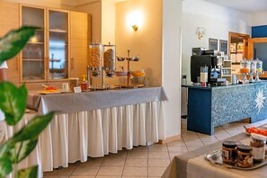 Ett område med en frukostbuffé som erbjuder ett stort utbud av mat, en kaffestation och en disk med olika drycker.
