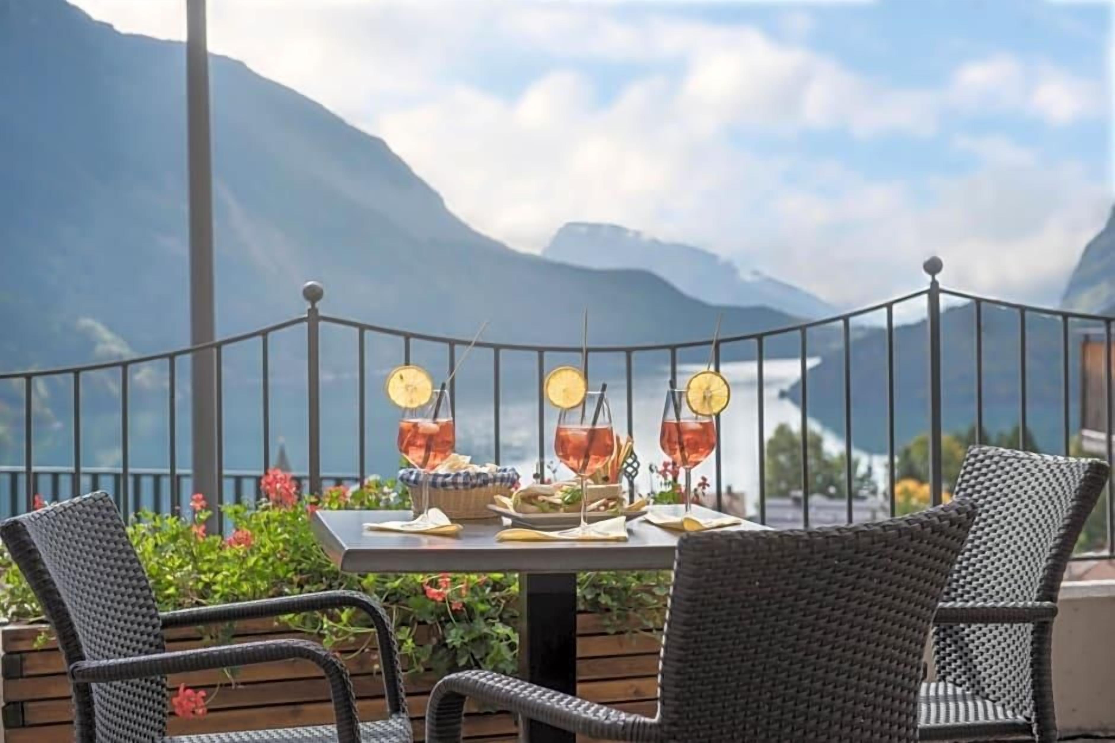 A table set with drinks and a sandwich, overlooking a mountainous landscape.