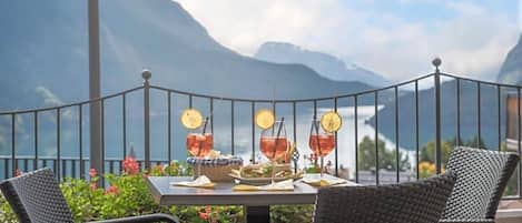 A table set with drinks and a sandwich, overlooking a mountainous landscape.