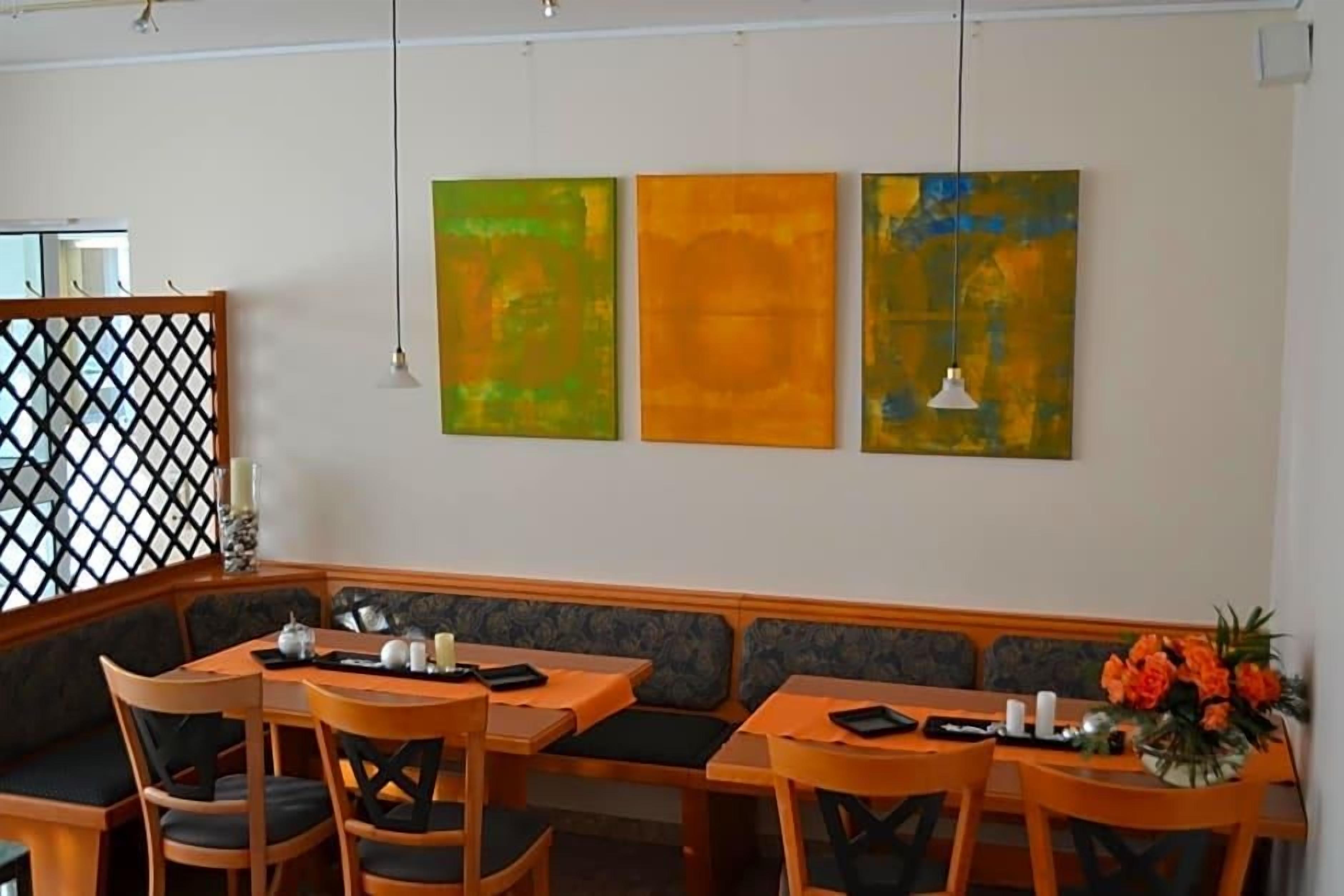Ein Restaurantinneres mit einer langen Theke, Holzkreisen und Tischen. An der Wand befinden sich drei abstrakte Gemälde.