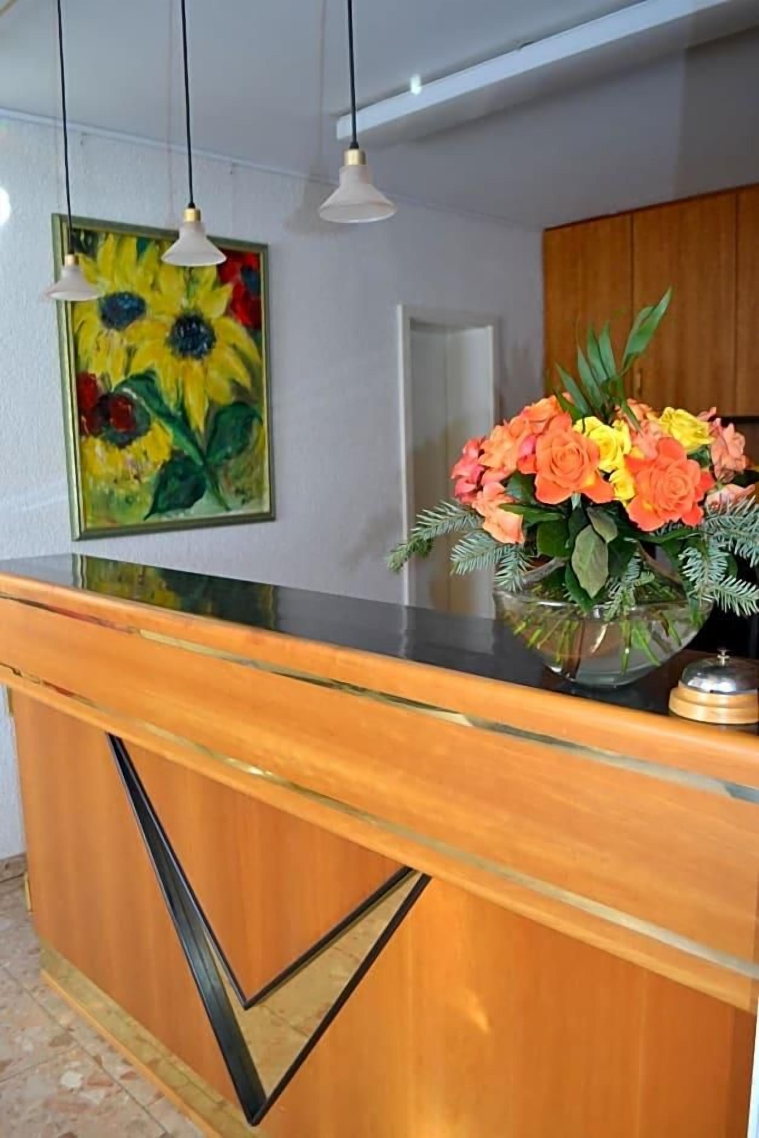 Ein Empfangsschalter mit Glastisch, ein Sonnenblumenbild und eine Blumenvase.