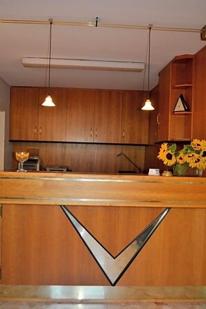 A wooden reception desk with a checkmark design, a vase of sunflowers, and a clock on the wall. - Aparthotel Sprendlingen (Sprendlingen)
