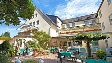 Ein Terrassenbereich im Freien mit Tischen und Stühlen, umgeben von Gebäuden und Pflanzen.