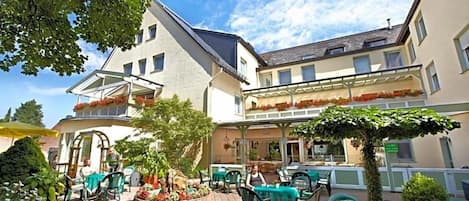 An outdoor patio area with tables and chairs, surrounded by buildings and greenery.