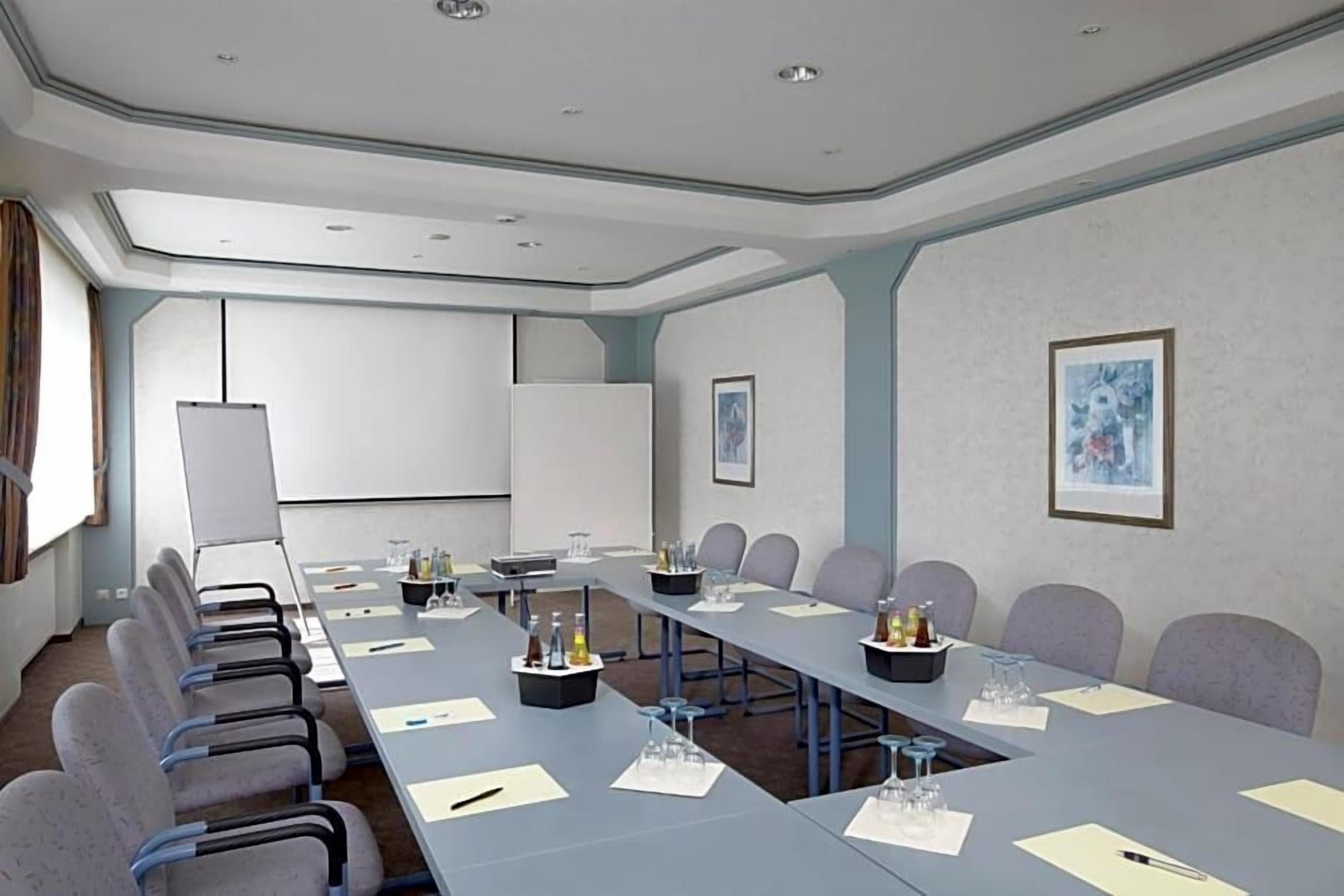 Ein Konferenzraum mit einem langen Tisch, Stühlen, einer Projektionsleinwand und gerahmten Kunstwerken an den Wänden.