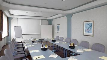 Ein Konferenzraum mit einem langen Tisch, Stühlen, einer Projektionsleinwand und gerahmten Kunstwerken an den Wänden.