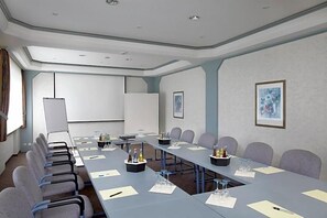 A conference room with a long table, chairs, a projector screen, and framed artwork on the walls. - Hotel Lindenhof (Warstein)
