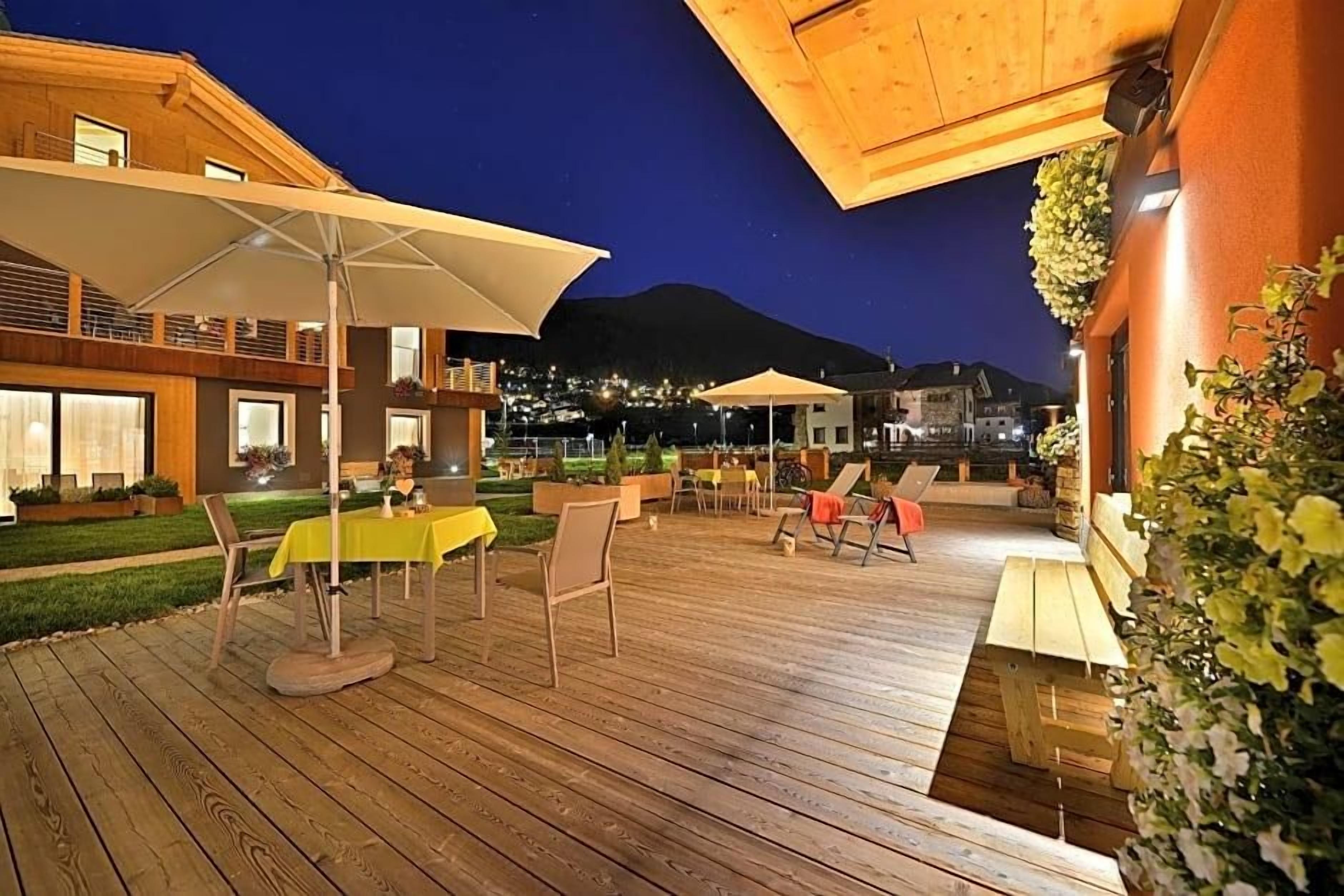 An outdoor patio area with wooden flooring, tables, chairs, and umbrellas.