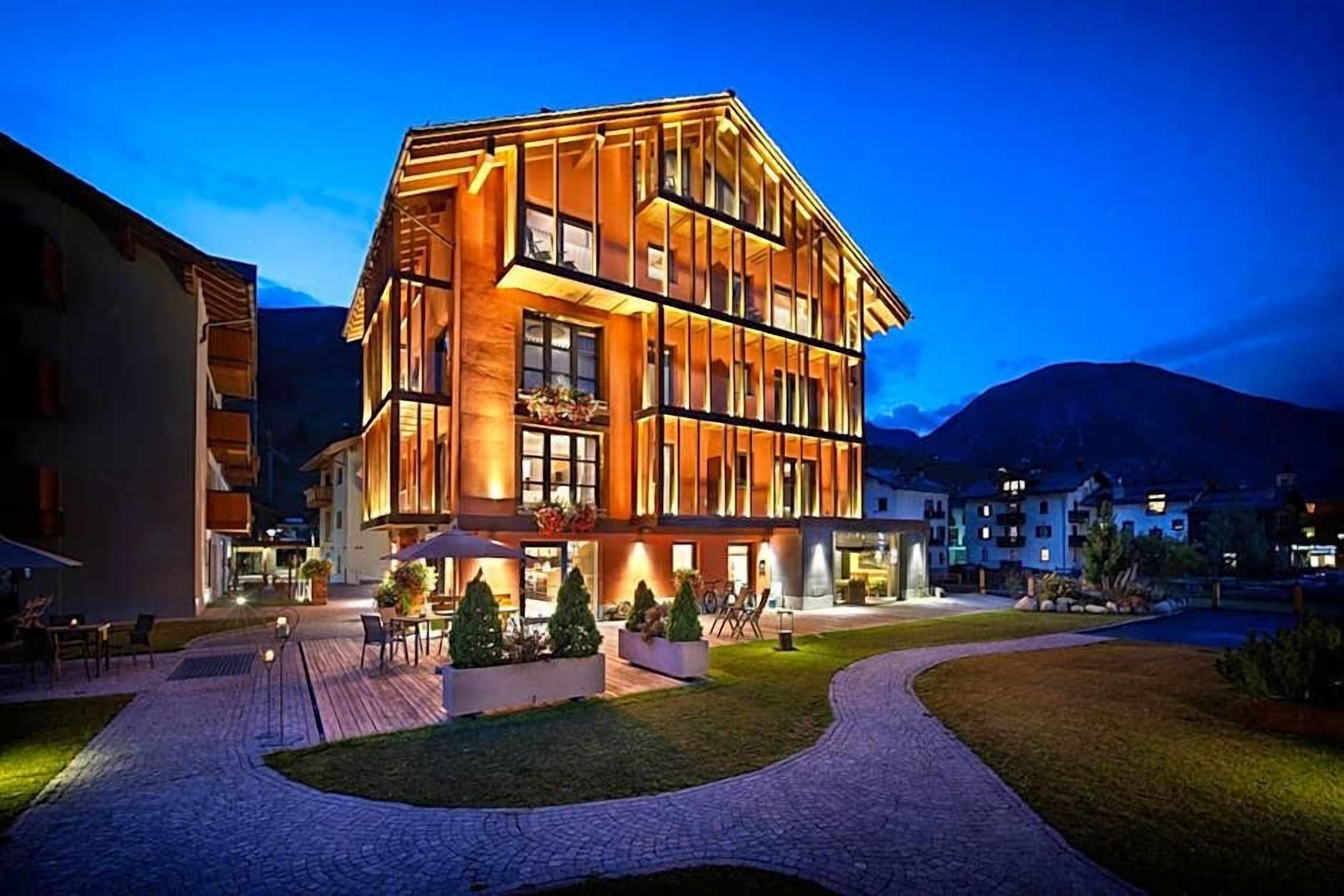 A multi-story hotel with a modern design, featuring a courtyard with outdoor seating and a well-lit entrance.