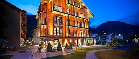 Un hotel de varios pisos con un diseño moderno, que cuenta con un patio con asientos exteriores y una entrada bien iluminada.