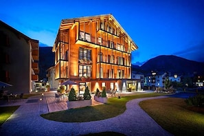 Un hotel de varios pisos con un diseño moderno, que cuenta con un patio con asientos exteriores y una entrada bien iluminada.