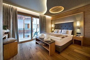 Habitación de hotel con una cama grande, un banco de madera, una mesita de noche y vistas al exterior.