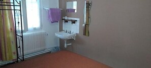 A bathroom with a white sink, a mirror, a radiator, and a window with curtains. - Le Parisien (Saintes)