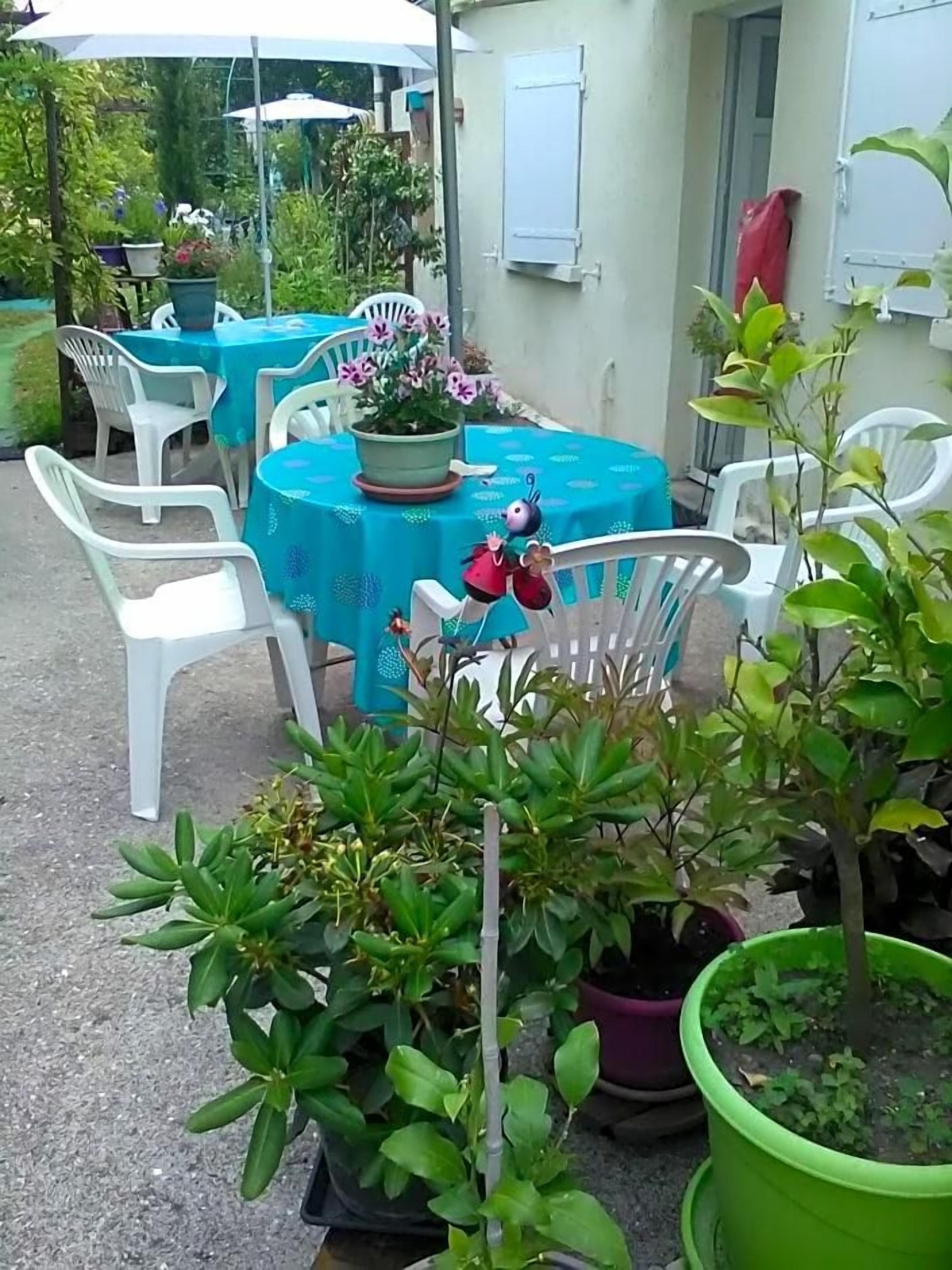 An outdoor patio area with tables and chairs, potted plants, and a small garden.