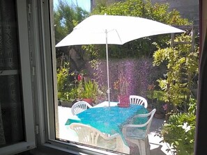 A patio with a table and chairs under a white umbrella, surrounded by greenery. - Le Parisien (Saintes)
