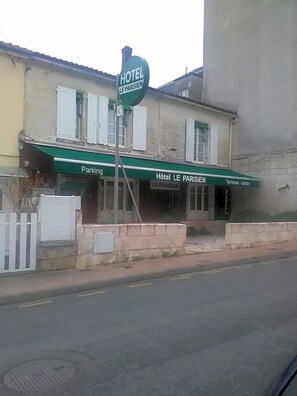 Hotel chamado 'Hotel Le Parisien' com toldo verde, placa indicando estacionamento e  área de terraço-jardim.