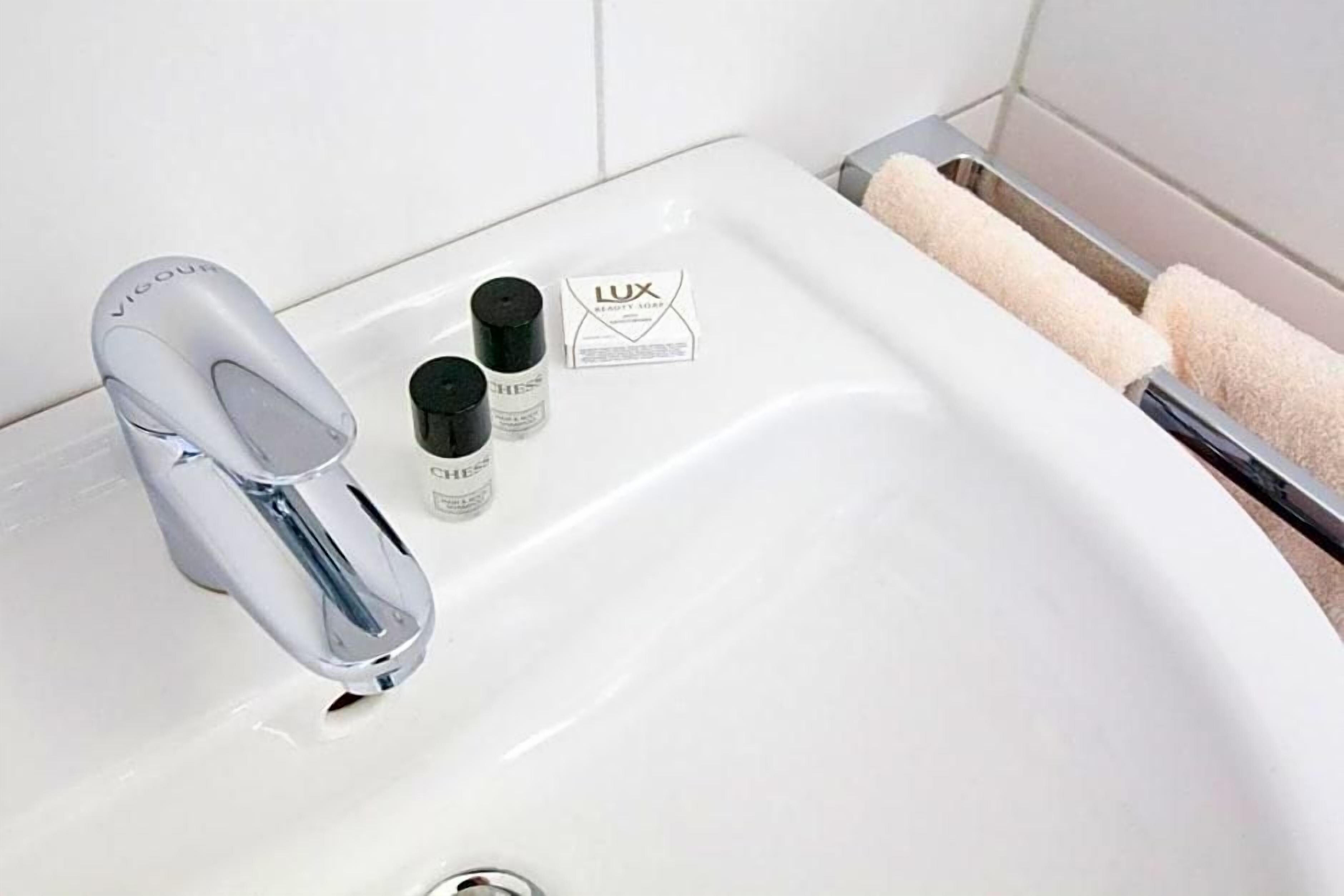 Ein Waschtisch mit einem modernen Wasserhahn, einem Taschentuchhalter und zwei Lotionflaschen.