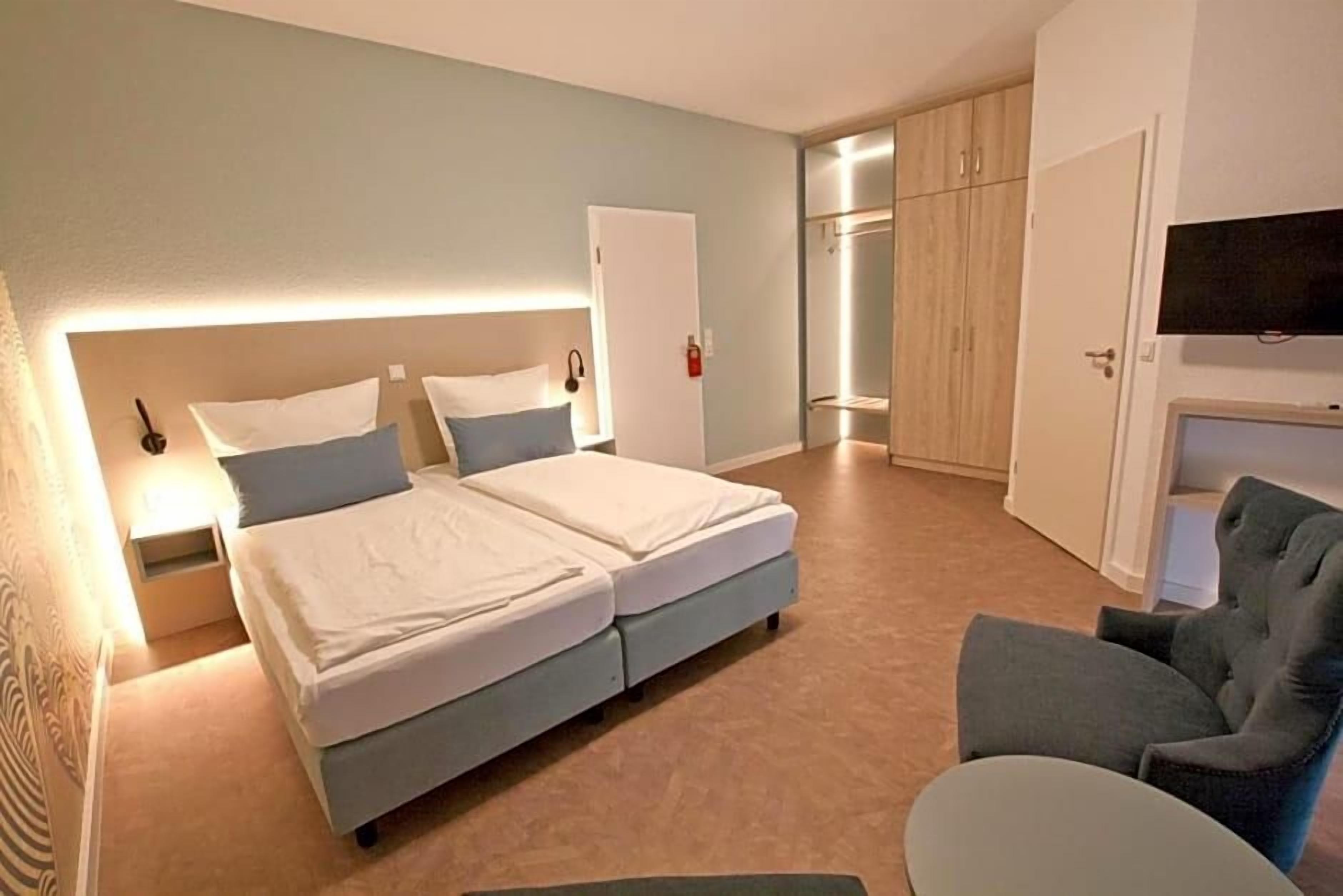 Ein Hotelzimmer mit einem Doppelbett, einem Sessel, einem Fernseher und einem Kleiderschrank.