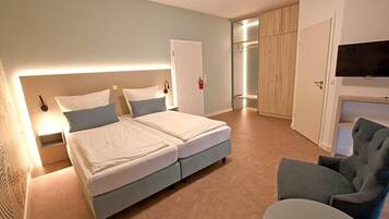 Ein Hotelzimmer mit einem Doppelbett, einem Sessel, einem Fernseher und einem Kleiderschrank.