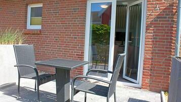 Un patio al aire libre con una mesa, sillas, una puerta corrediza de vidrio y una pared de ladrillo.