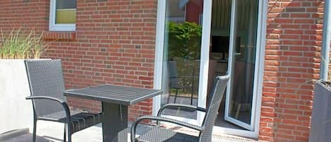 Un patio al aire libre con una mesa, sillas, una puerta corrediza de vidrio y una pared de ladrillo.