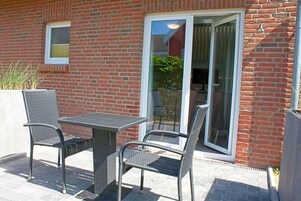 Un patio al aire libre con una mesa, sillas, una puerta corrediza de vidrio y una pared de ladrillo.