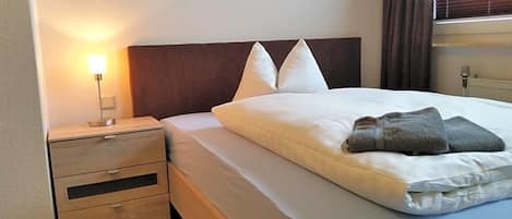 A hotel room with a bed, pillows, a bedside lamp, and a nightstand.