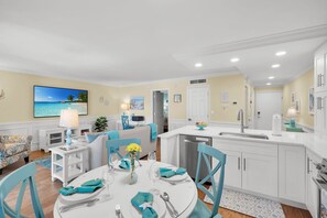 Een ruime, moderne keuken met witte kasten, een centraal keukenblok met spoelbak en een eetgedeelte met een ronde tafel gedekt voor vier personen.