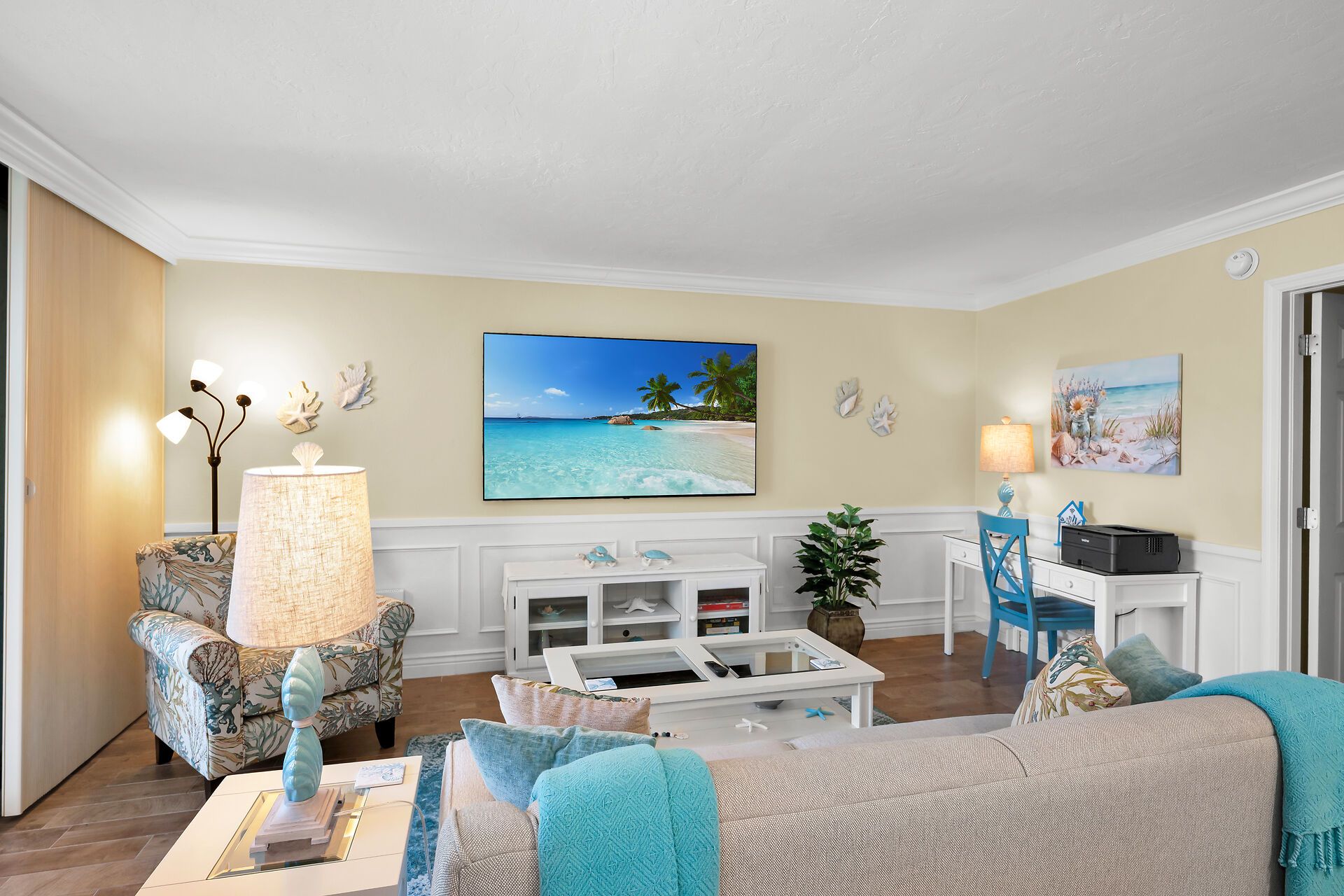 A living room with a beach-themed painting, a white entertainment unit, and a blue chair.