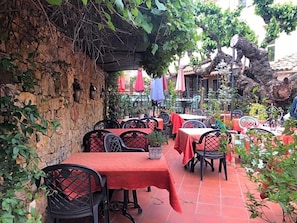 An outdoor café with tables and chairs, a stone wall, and potted plants. - Le Provenvßal (Aups)