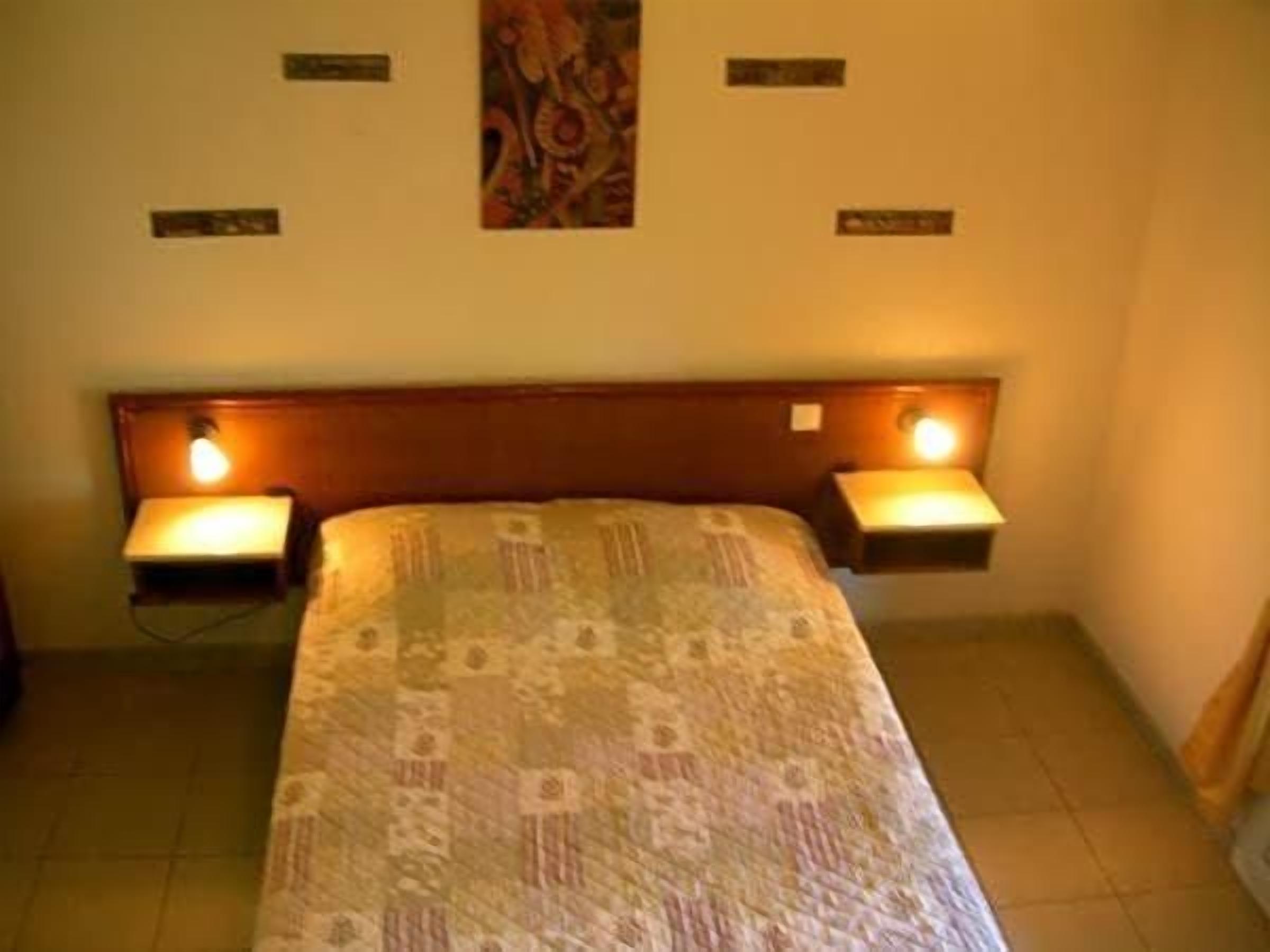 A hotel room with a bed, two bedside tables with lamps, a headboard, and a wall-mounted artwork.