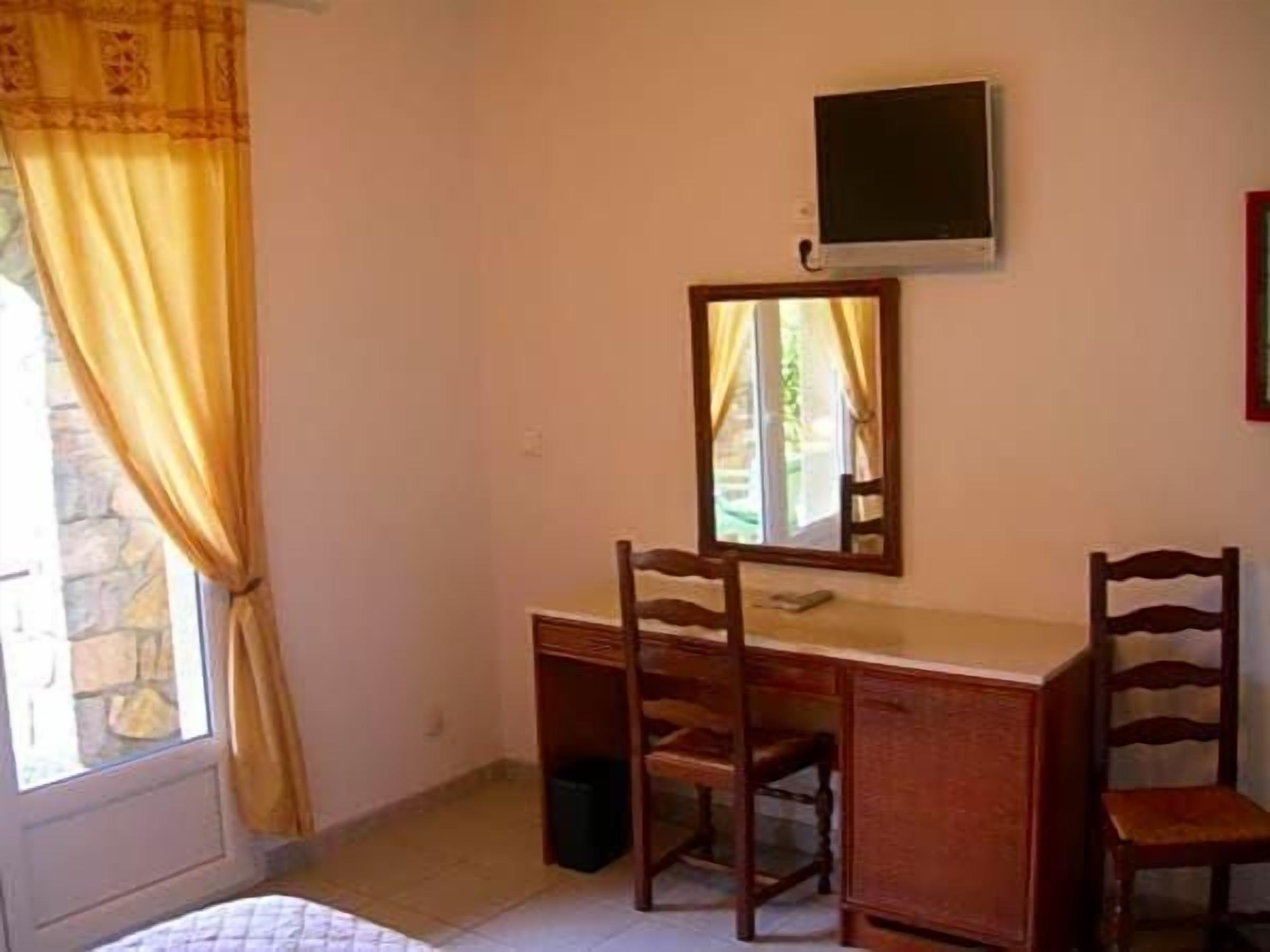 Una habitación con escritorio, dos sillas, televisor y ventana con cortinas.