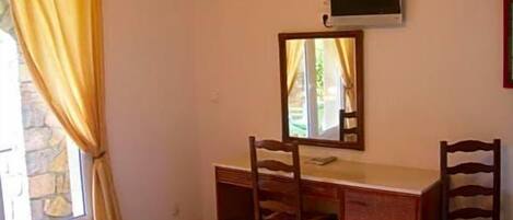 A room with a desk, two chairs, a television, and a window with curtains.