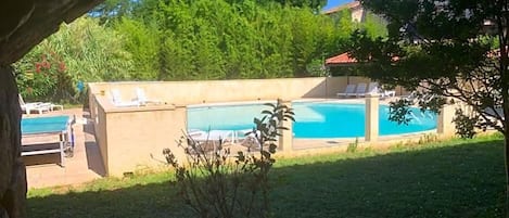 A backyard with a swimming pool, lounge chairs, and a stone structure.