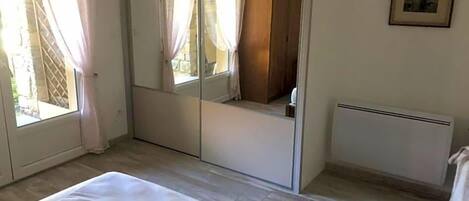 A bedroom with a bed, a large mirror, a radiator, and a window with curtains.