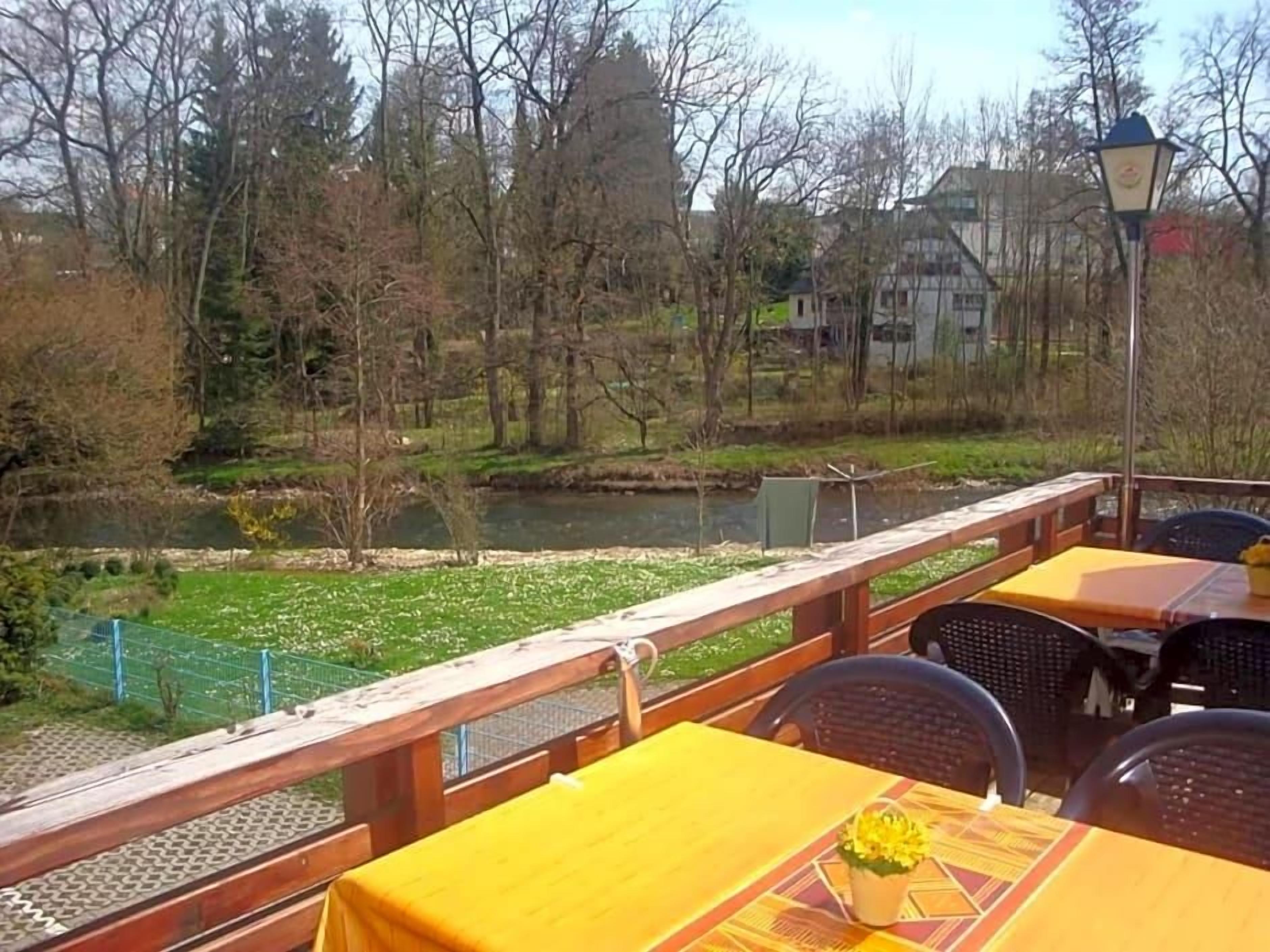 A terrace with tables and chairs, overlooking a river and trees.