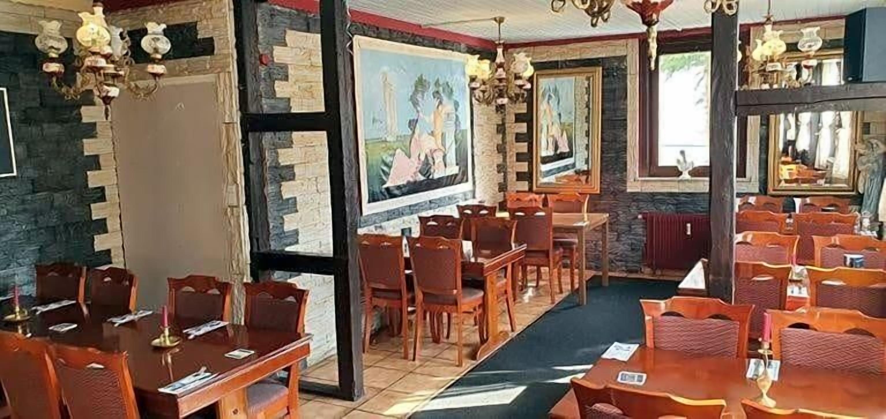 Ein Restaurant mit mehreren Tischen, Stühlen, einer Kristallleuchtre und gerahmten Kunstwerken an den Wänden.