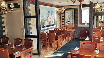 Ein Restaurant mit mehreren Tischen, Stühlen, einer Kristallleuchtre und gerahmten Kunstwerken an den Wänden.
