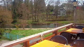 Eine Terrasse mit Tischen und Stühlen mit Blick auf einen Fluss und Bäume.