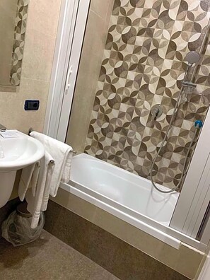 Un baño con ducha, lavabo y toallero.